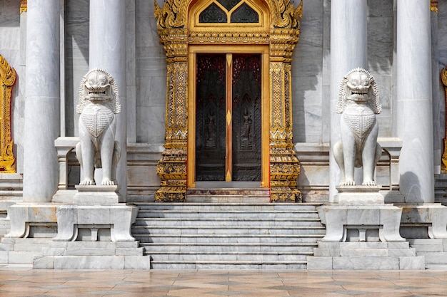 Coppia di leoni di marmo davanti alla porta di Wat Benchamabophit Dusit Wanaram Questo tempio è conosciuto come il tempio di marmo a Bangkok cielo blu e nuvole Uno dei templi più belli della Thailandia