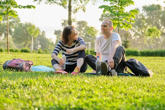 Coppia di mezza età che si siede sulla stuoia di yoga, uomo e donna che parlano acqua potabile rilassante. Stile di vita sano attivo, relazione, sport, fitness nelle persone mature