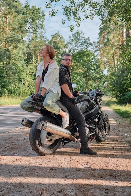 Coppia di mezza età parlando e divertendosi seduti su una moto che viaggiano insieme su una strada forestale