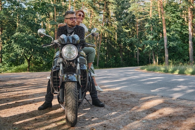 Coppia di mezza età parlando e divertendosi seduti su una moto che viaggiano insieme su una strada forestale