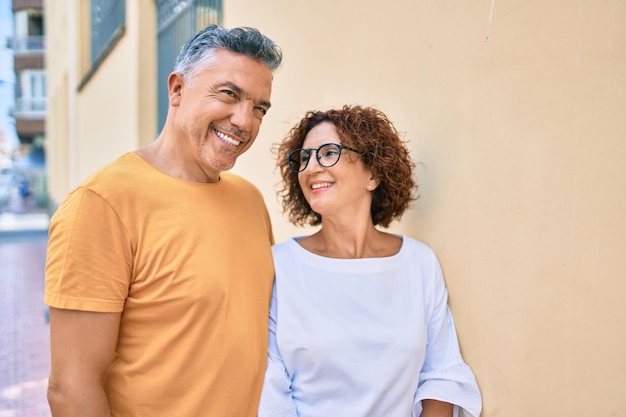 Coppia di mezza età sorridente felice appoggiata al muro in strada della città