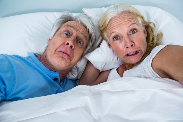 Coppia di pensionati facendo facce mentre si rilassano sul letto