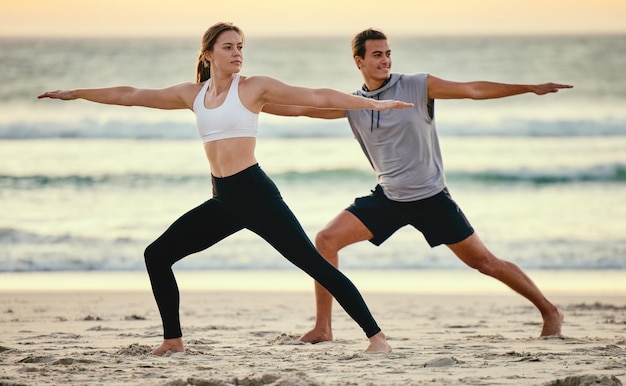 Coppia di posa del guerriero e yoga sulla spiaggia al tramonto per la salute, il fitness e il benessere Esercizio zen chakra e uomo e donna che allungano l'allenamento e praticano pilates per l'equilibrio all'aperto in riva al mare