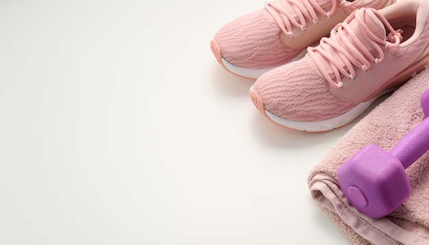 Coppia di scarpe da ginnastica rosa, un asciugamano di spugna e un manubrio di plastica su uno sfondo bianco, vista dall'alto, spazio per le copie