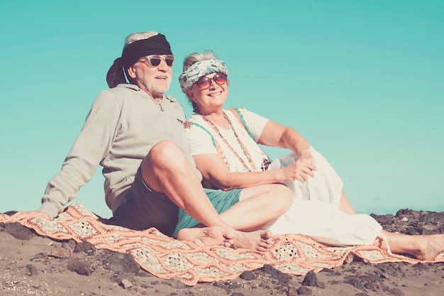 coppia di senior hippy caucasico stile e vita riposano sulla spiaggia rocciosa di tenerife. colori e stile di vita alternativo per un concetto di totale libertà vicino all'oceano.. felicità per persone simpatiche e allegre