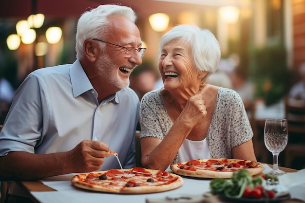 Coppia di signori anziani con i capelli bianchi sorridono mentre mangiano una pizza Festeggiamo l'anniversario in pizzeria seduti all'aperto Concetto di persone felici