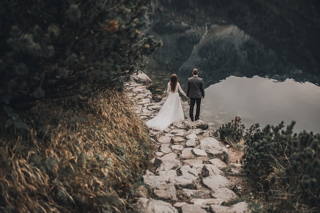 coppia di sposi dalla carnagione chiara In abiti da sposa. un grande lago trasparente e pietre grigie e alberi