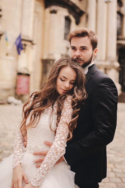 Coppia di sposini felici abbracciare e baciare nella vecchia strada della città europea, splendida sposa in abito da sposa bianco insieme allo sposo bello. giorno del matrimonio.