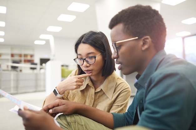 Coppia di studenti internazionali che discutono di documenti mentre si lavora al progetto nella biblioteca del college