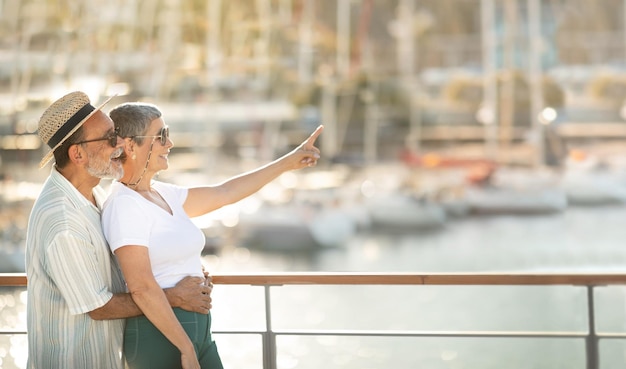 Coppia di turisti senior che punta il dito nello spazio libero al porto turistico