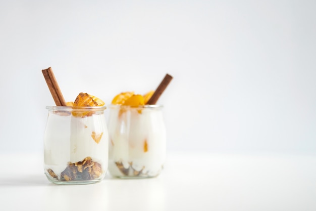 Coppia di vasetti di vetro di yogurt greco con muesli, cannella e albicocche in scatola