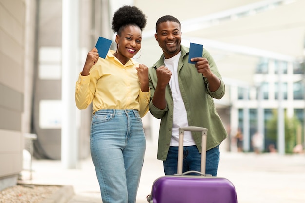 Coppia di viaggiatori neri che gesticolano Sì in possesso di passaporti vicino all'aeroporto all'aperto