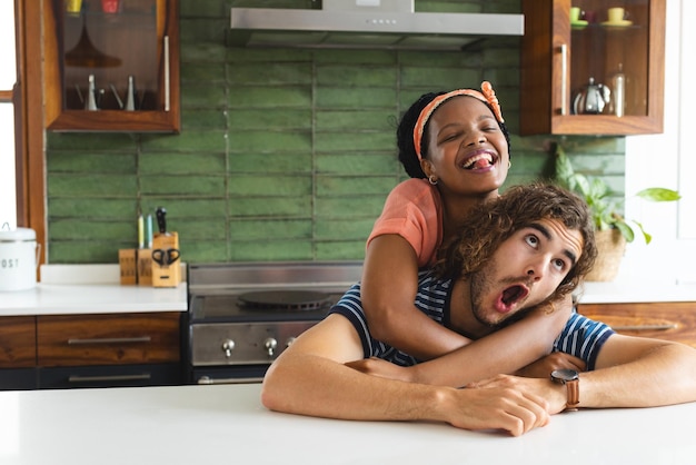 Coppia diversificata giovane donna afroamericana abbraccia un giovane uomo caucasico da dietro in una cucina