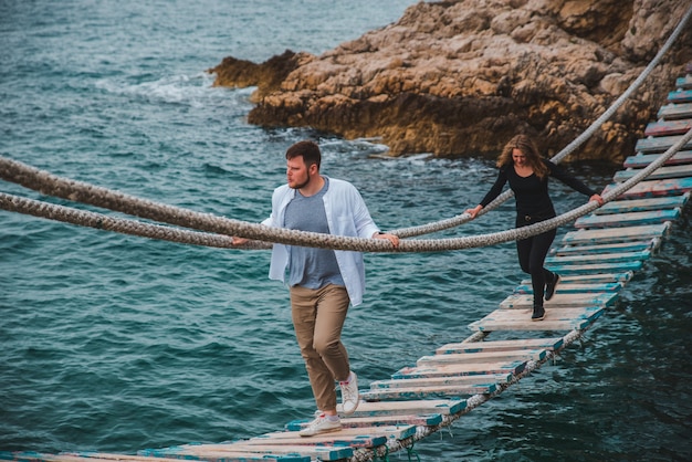 Coppia donna con uomo che cammina dal ponte sospeso traballante che attraversa la baia del mare divertendosi