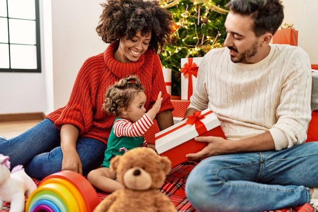 Coppia e figlia che tengono regalo seduto vicino all'albero di Natale a casa