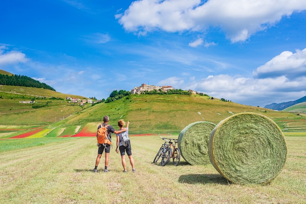 Coppia escursioni nei campi coltivati in fiore degli altopiani di Castelluccio di Norcia, famosa pianura fiorita colorata nell'Appennino, Italia. Agricoltura di colture integrali e papaveri rossi.