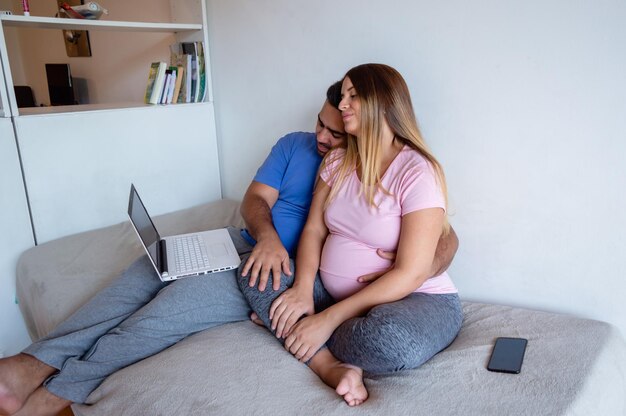 coppia eterosessuale incinta seduta sul letto utilizzando il computer portatile