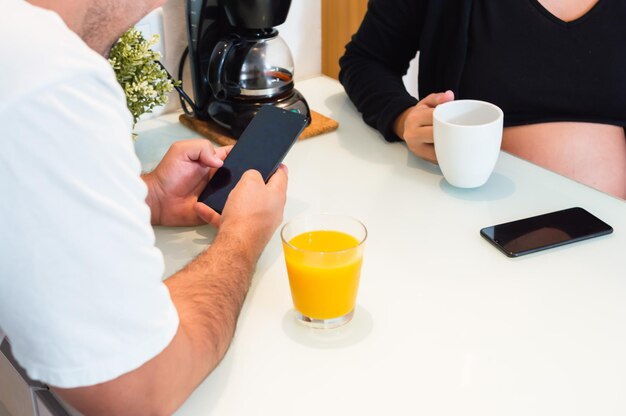 coppia eterosessuale irriconoscibile attorno al tavolo a casa a bere succo di frutta e usare il telefono