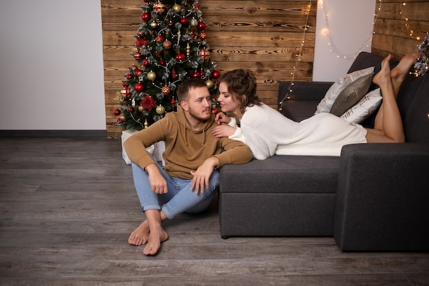 Coppia felice a casa sul divano. Albero di Natale sullo sfondo.