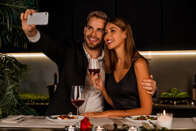 Coppia felice a cena e prendendo selfie utilizzando lo smartphone all'interno