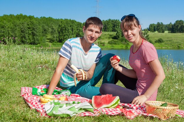 Coppia felice al picnic sul lago a mangiare frutti, divertirsi insieme. ritratto all'aperto