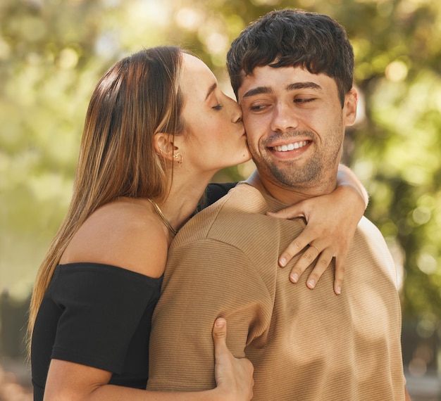 Coppia felice amore e bacio sulla guancia all'aperto nel parco naturale per vacanze avventurose e tempo di qualità insieme in estate Impegno sicurezza e aria fresca per un matrimonio sano con un uomo e una donna