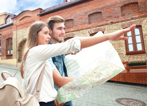 Coppia felice che cammina all'aperto per visitare la città e tiene in mano una mappa.