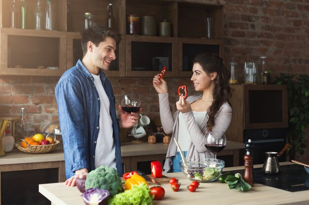 Coppia felice che cucina insieme cibo sano nella loro cucina soppalcata a casa. Donna e uomo che bevono vino. Preparazione dell'insalata di verdure.