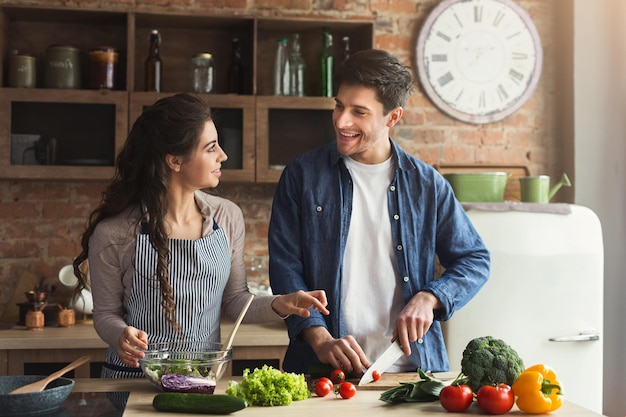 Coppia felice che cucina insieme una cena sana nella loro cucina soppalcata a casa. Preparazione insalata di verdure e incontro, fine settimana in famiglia, spazio copia