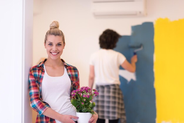 Coppia felice che fa lavori di ristrutturazione a casa, l'uomo sta dipingendo la stanza e la donna tiene il vaso con i fiori