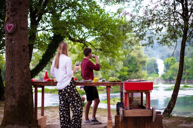 coppia felice che fa picnic con cena francese all'aperto durante le vacanze estive vicino al fiume in una natura meravigliosa