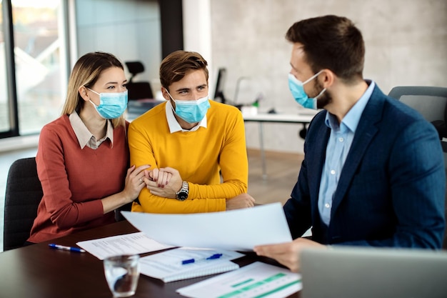 Coppia felice che indossa maschere facciali mentre ha un incontro con un consulente finanziario in ufficio