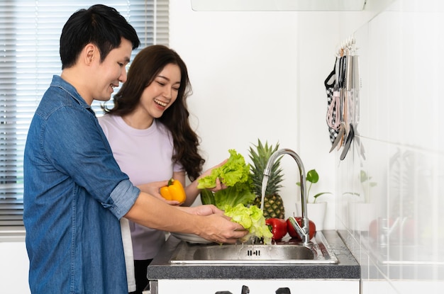 Coppia felice che lava le verdure nel lavandino in cucina a casa cucinando insieme