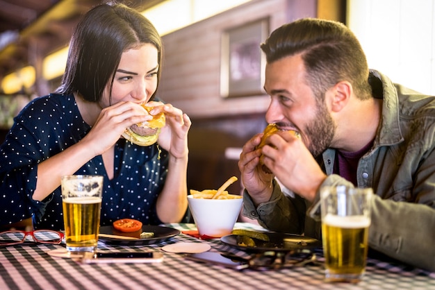 Coppia felice che si diverte a mangiare hamburger al ristorante pub fast food