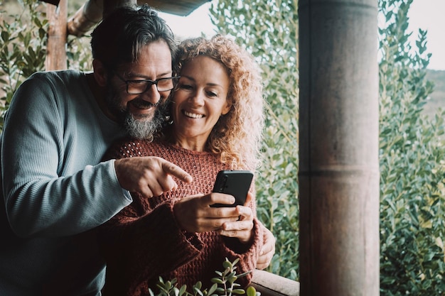 Coppia felice che usa il cellulare per divertirsi insieme fuori sulla terrazza di casa L'uomo e la donna sorridono e usano il cellulare per videochiamare e comunicare all'aperto Tecnologia e stile di vita delle persone