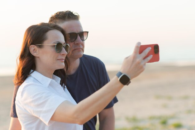 Coppia felice con differenza di età, una giovane donna e un uomo di mezza età si fanno un selfie sulla spiaggia