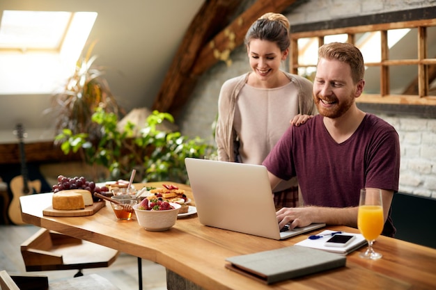 Coppia felice con laptop dopo colazione nella sala da pranzo