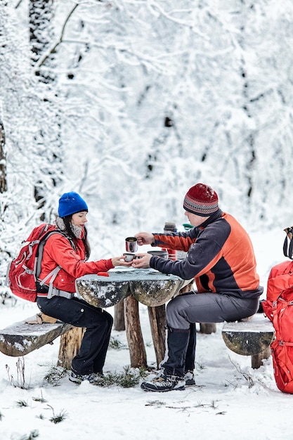 Coppia felice davanti a un falò nella foresta innevata d'inverno