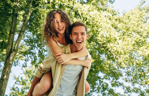 Coppia felice divertendosi fuori nel parco Fidanzato che fa un giro sulle spalle alla sua bella ragazza in una vacanza estiva sulla natura