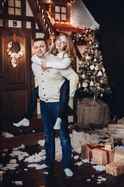 coppia felice in interni di Natale. Uomo che dà la sua ragazza sulle spalle giro.