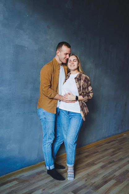 Coppia felice innamorata vestita di camicie in piedi sullo sfondo del muro grigio guardando lo spazio vuoto sfondo isolato del muro di cemento grigio Il concetto di una coppia felice innamorata