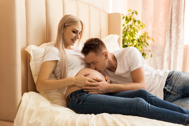 Coppia felice. Madre incinta e marito che baciano neonato attraverso la pancia della moglie a casa