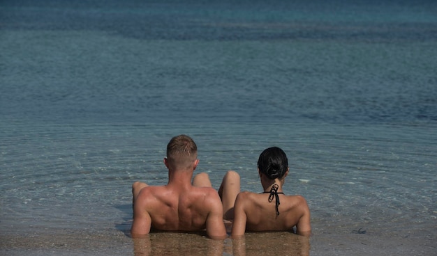 Coppia felice rilassante, abbronzandosi sulla spiaggia, sdraiato in acqua, guardando l'oceano, copyspace. Luna di miele e concetto di vacanza. Coppia innamorata che si rilassa in vacanza, luna di miele. I giovani amanti nuotano in mare.