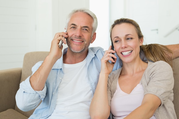 Coppia felice seduto sul divano a parlare sui loro telefoni