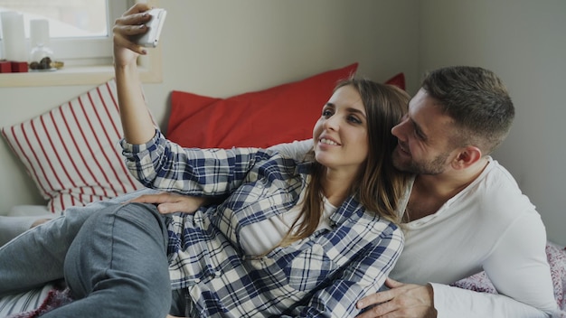Coppia felice sposata che prende selfie mentre si trova sul letto a casa al mattino