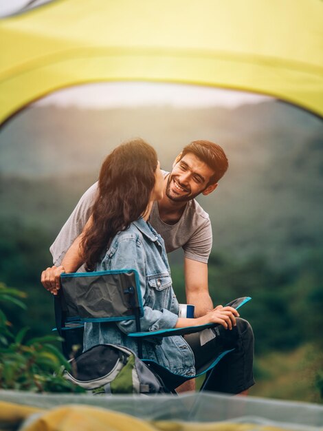 Coppia felice uomo e donna seduti su una sedia davanti alla tenda da campeggio al campeggio al mattino