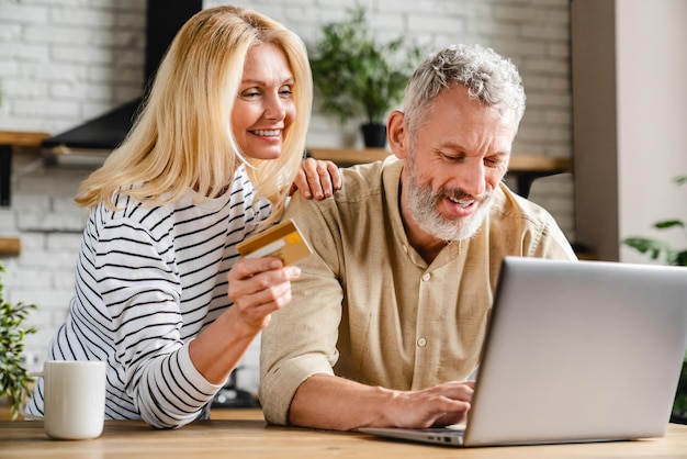 Coppia felice utilizzando la carta di credito per lo shopping online utilizzando il laptop