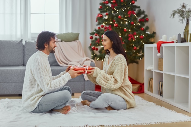 Coppia festeggia il capodanno vicino all'albero di Natale a casa regala regali nelle scatole regalo