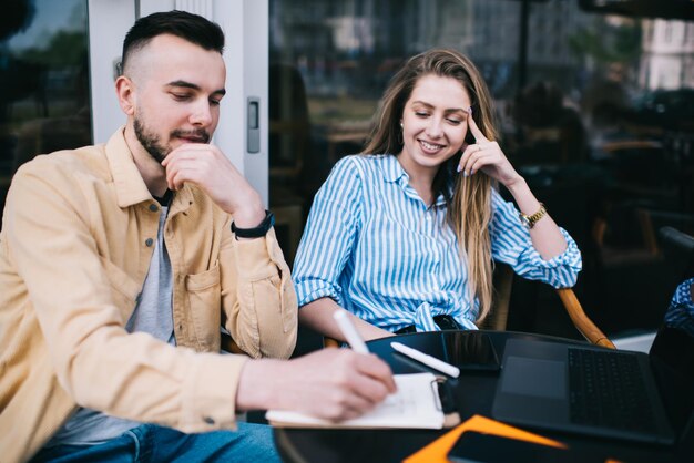 Coppia freelance scrivendo negli appunti e navigando nel laptop in caffetteria