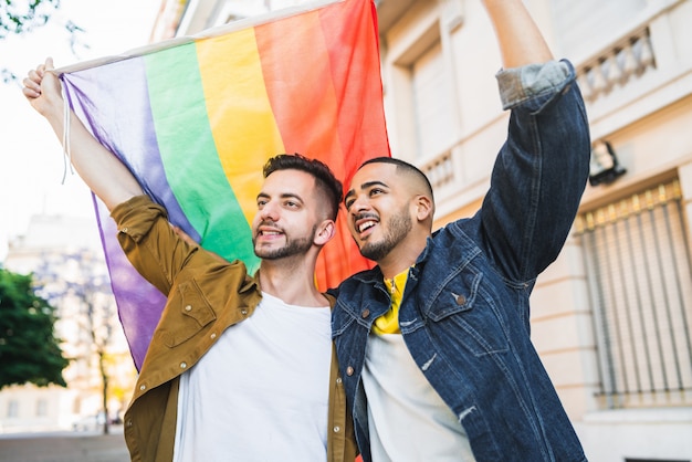 Coppia gay abbracciando e mostrando il loro amore con la bandiera arcobaleno.